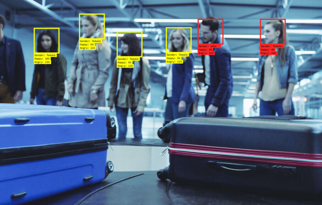 Facial recognition software identifying individuals next to a baggage collection carousel in an airport.