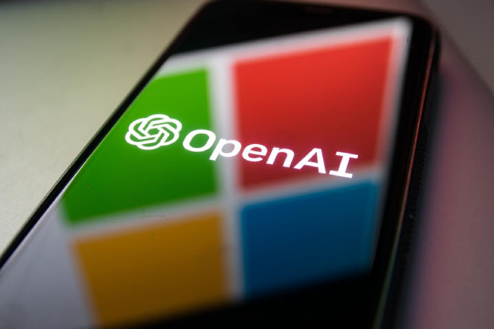 OpenAI logo on the phone and Microsoft logo reflection.