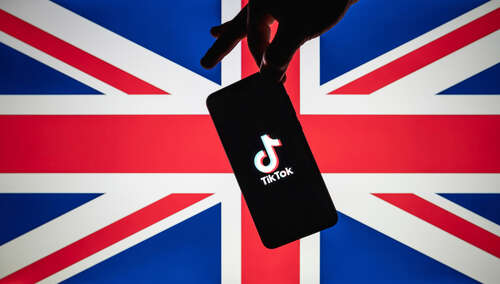 An image of TikTok logo on a smartphone, being held by pincer grip in front of a UK flag.