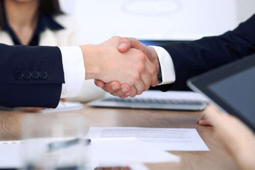 Two hands shaking over a paper contract on a table.
