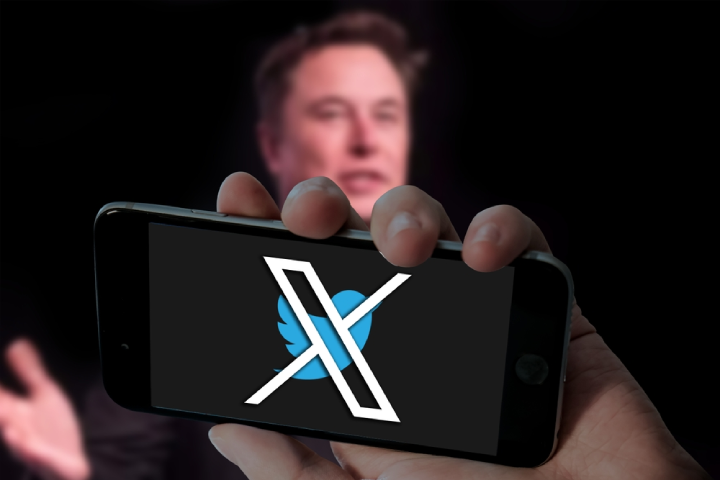 Twitter X with bird logo in holding mobile and Elon musk picture in blurred laptop screen background.