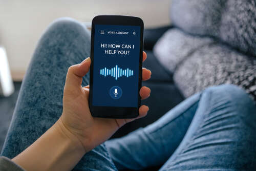 An image of someone holding their phone. The voice assistant asks on the screen "How can I help you?"