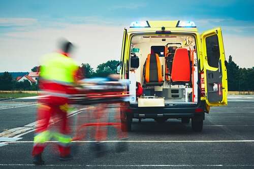 An emergency services technician is pushing a bed trolley to an ambulance. His image is blurred, distorting him from reality. 