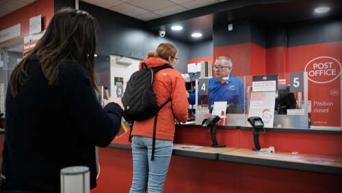 A UK Post Office counter with people queuing. 