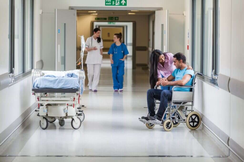 A doctor attends to a patient in a wheelchair in an NHS hospital corridor, illustrating a story about Palantir's involvement in the NHS.