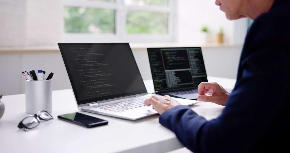 Photo of a woman reviewing code on two computer screens, illustrating a story about the burgeoning threat of AI malware to companies.