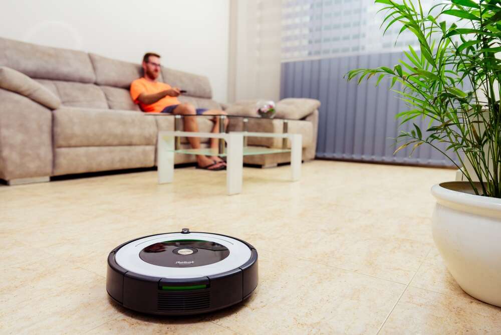A photo of a Roomba in a living room, used to illustrate a story about the defunct Amazon iRobot deal.