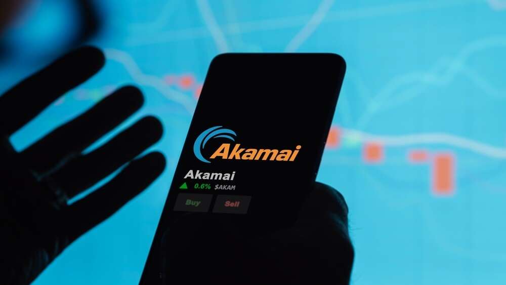 A man holding a mobile phone with the Akamai logo on its screen, used to illustrate a story about Akamai's Gecko platform.