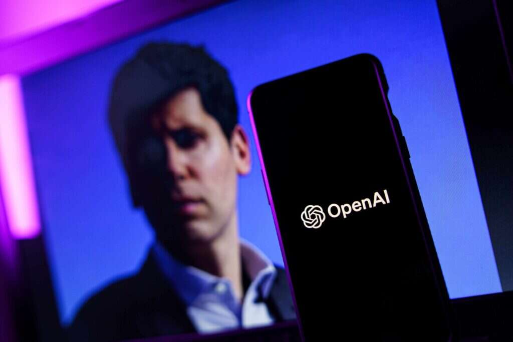 A phone showing the OpenAI logo and Sam Altman's photo in the background