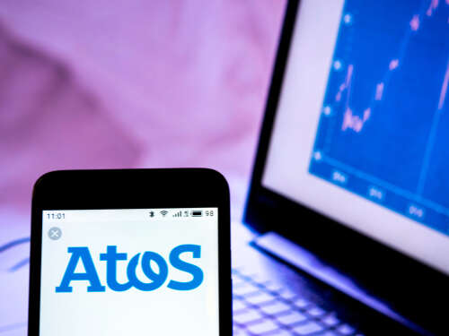 A photo of the Atos logo on a smartphone, with a graph on a laptop screen in the background.