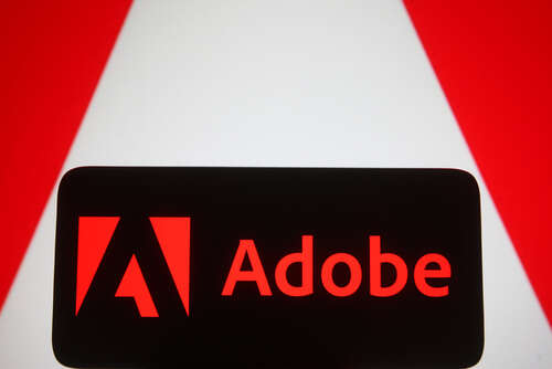 The Adobe logo on a mobile phone, backdropped by a larger version of the Adobe logo, used to illustrate a story about Adobe AI services. 
