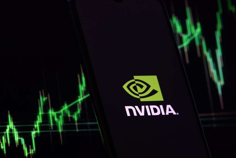 A photo of the Nvidia logo on a smartphone, backgrounded by a green line chart. The line is going up.